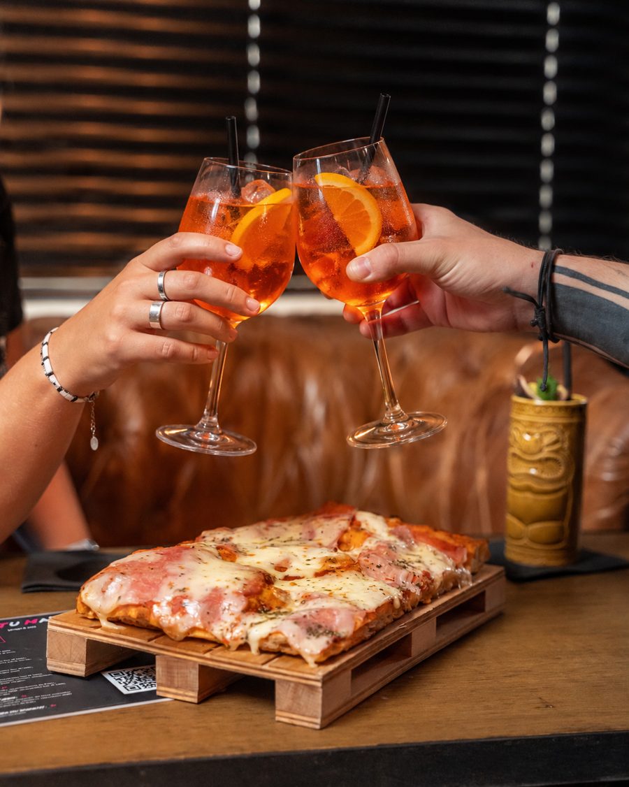 Deux Aperol Spritz qui trinquent au-dessus d'une pizza artisanale au Rambler Cocktail Club, Lyon